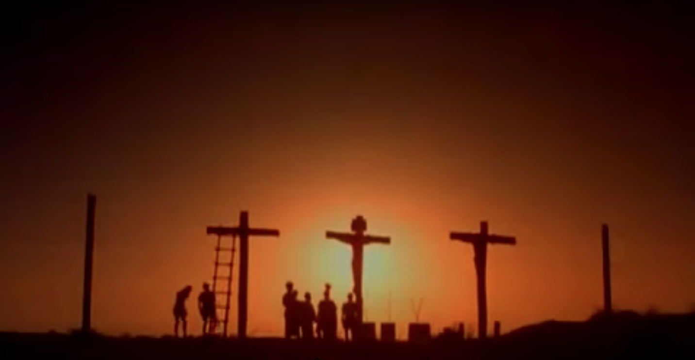 L'ombre de trois croix de crucifixion avec celle de Jésus au milieu. Des ombres de soldats et des Hommes en bas des croix sont présents