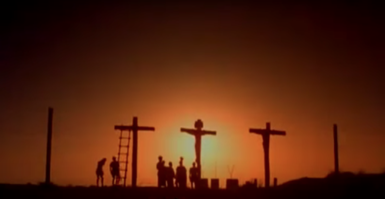 L'ombre de trois croix de crucifixion avec celle de Jésus au milieu. Des ombres de soldats et des Hommes en bas des croix sont présents