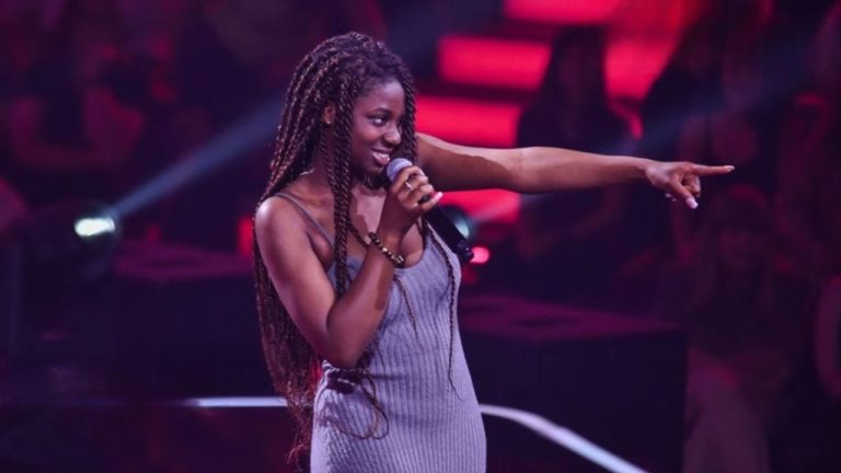 Desirey Sarpong Agyemang, micro en main, sur la scène de The Voice pointe le doigt vers le jury