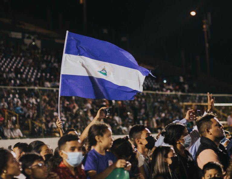 Des individus portant un masque rassemblés devant une scène, l'un porte un drapeau du Nicaragua