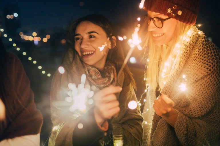 Deux femmes sont dehors, souriantes, avec des allumettes de bengales en main