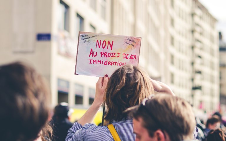 Au milieu d'autres manifestants, une femme lève une petite pancarte où est écrit: "Non au projet de loi immigration"