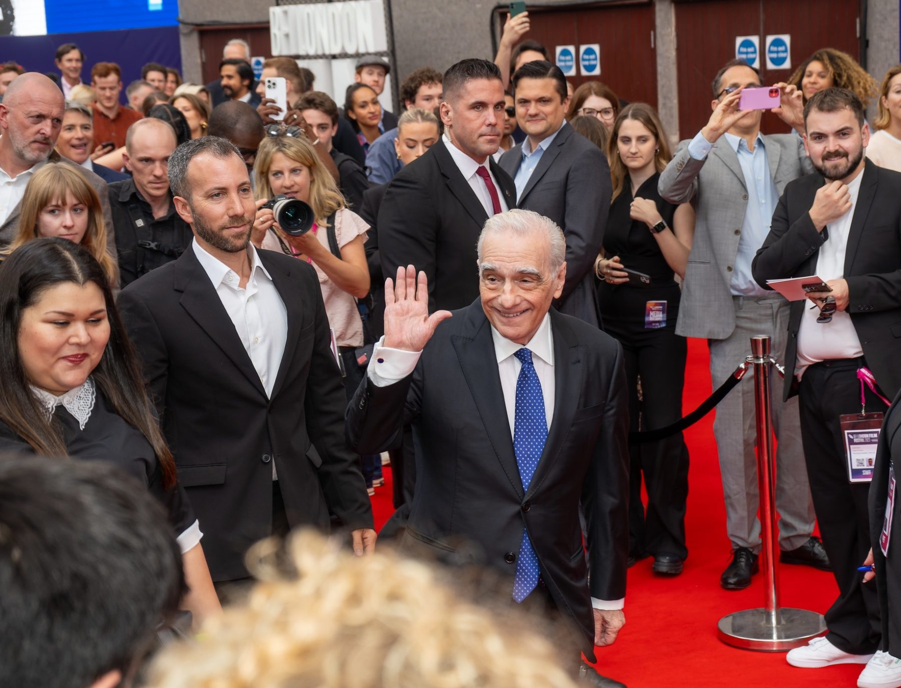 Martin Scorsese marche sur un tapis rouge et lève la main devant les photographes