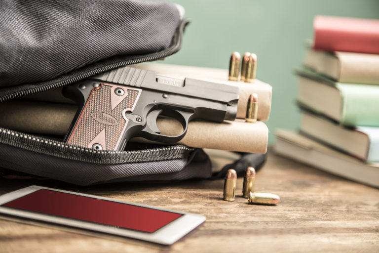 un pistolet et des balles sont dans un sac à dos avec des livres et un smartphone autour