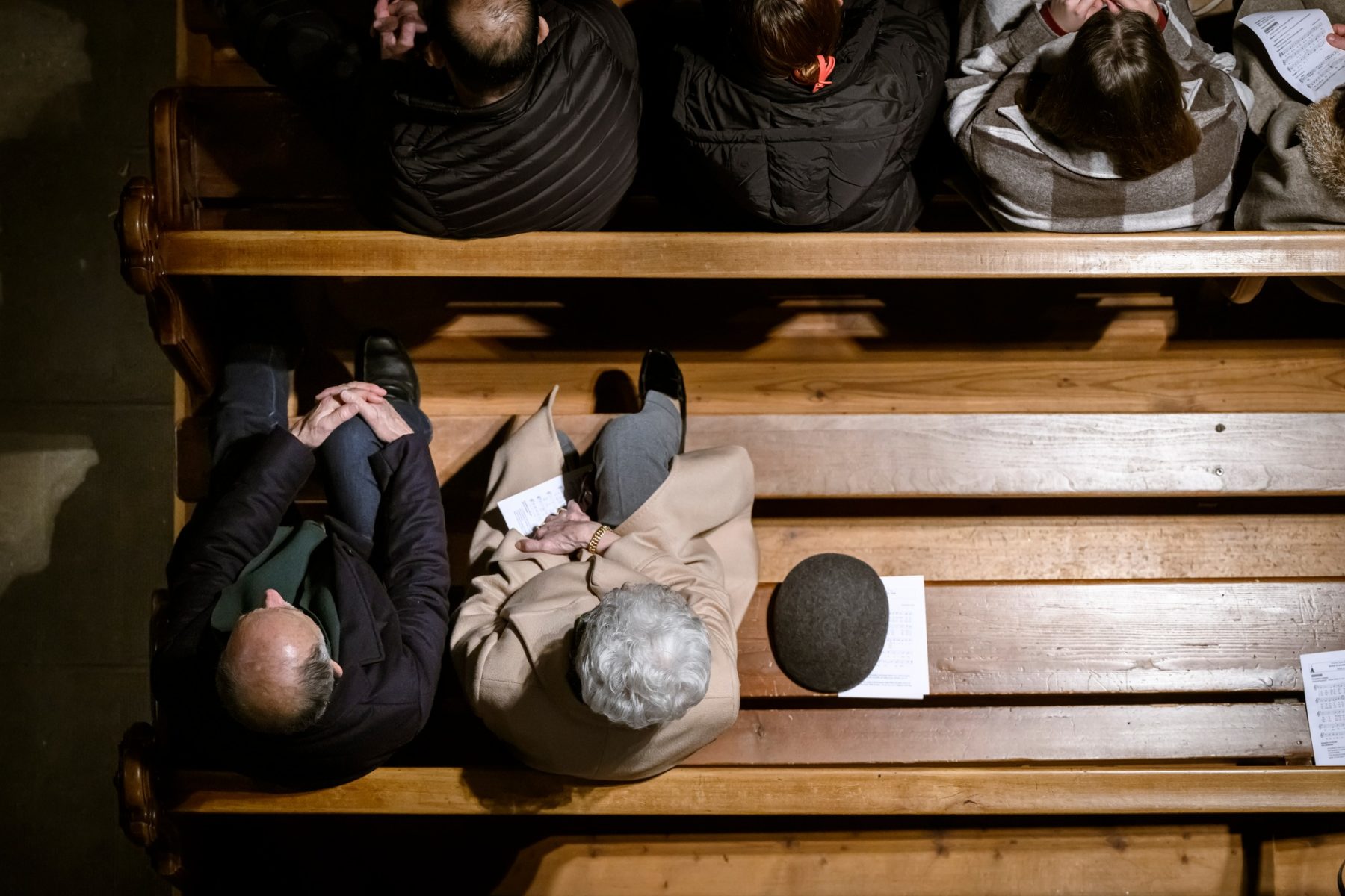 Vue d'en haut d'un banc d'église. 4 personnes sont assises sur le premier, 2 sur le second, 2 places vides à côté des deux autres personnes.