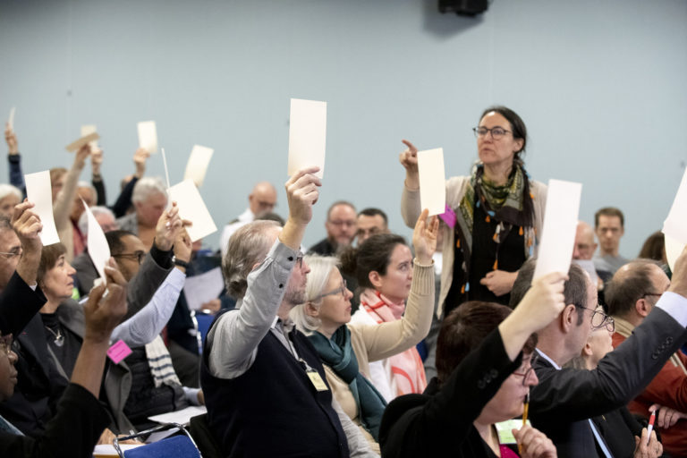 Les délégués votent en levant un morceau de carton en l'air. Une dame est en train de les compter.