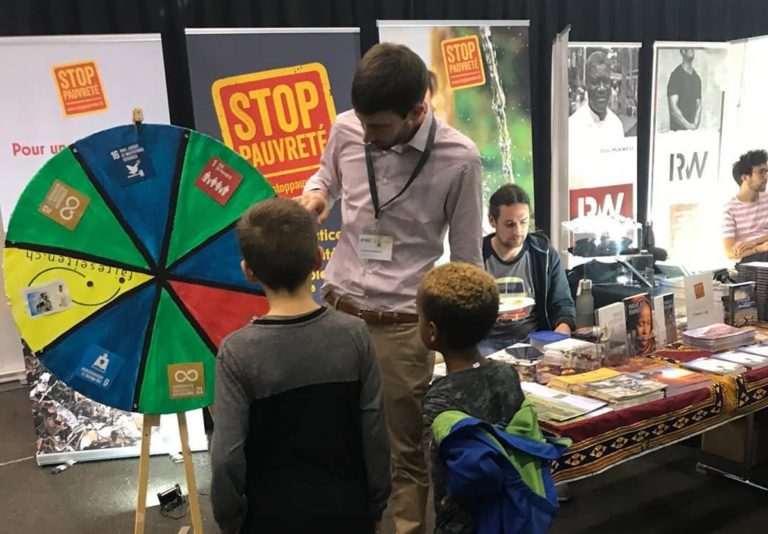 Alexis Bourgeois tient un stand StopPauvreté et deux enfants de dos font tourner une roue