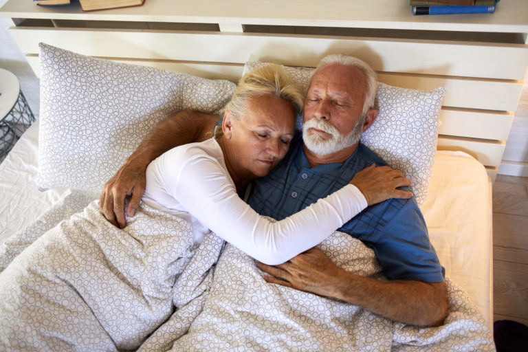 Un couple de personnes âgées endormies enlacées dans un lit