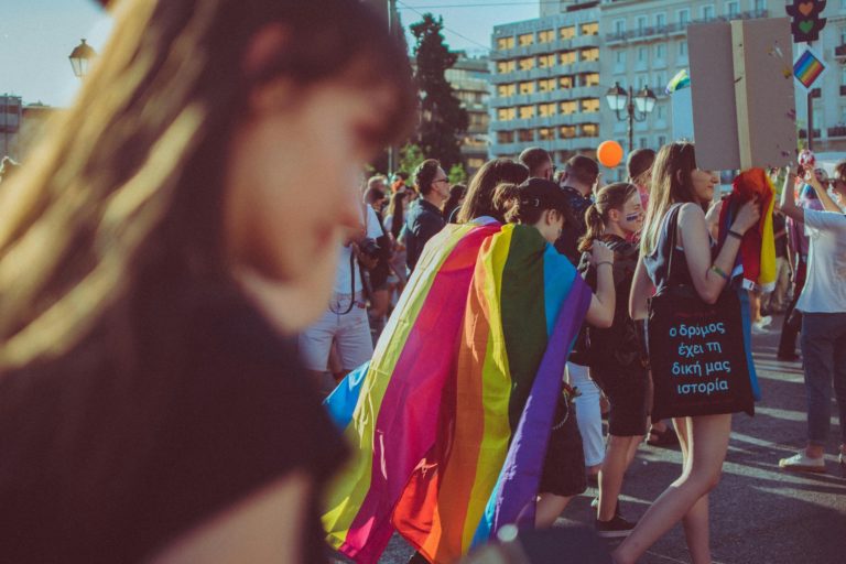 Des grecs marchent lors de la gay pride en Grèce avec un drapeau arc-en-ciel sur le dos