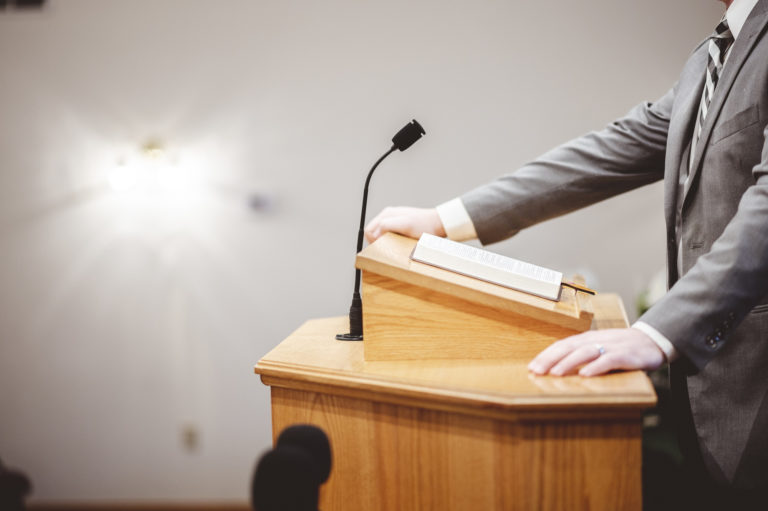 On ne voit qu'une chaire avec une bible ouverte. les mains d'un pasteur sont posées dessus.