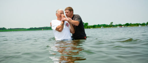 Une personne du troisième âge se bouche le nez avant de se faire baptiser dans un plan d'eau en plein air