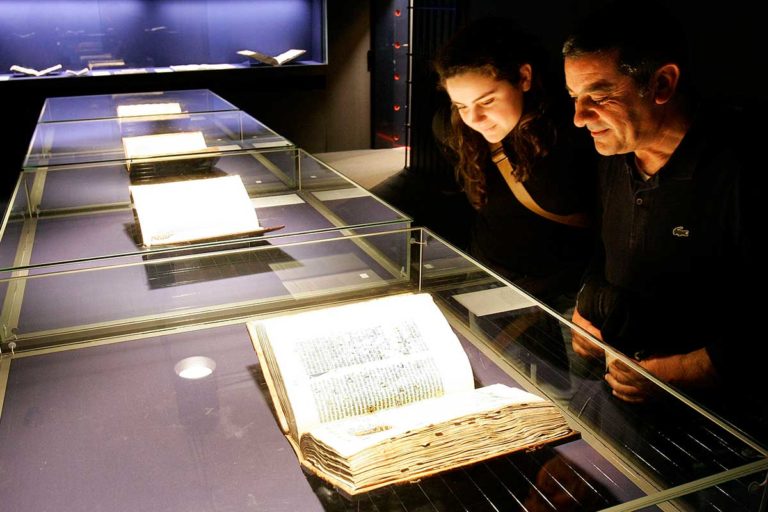 Une femme et un homme admire une Bible de Gutenberg protégée par une vitre en verre