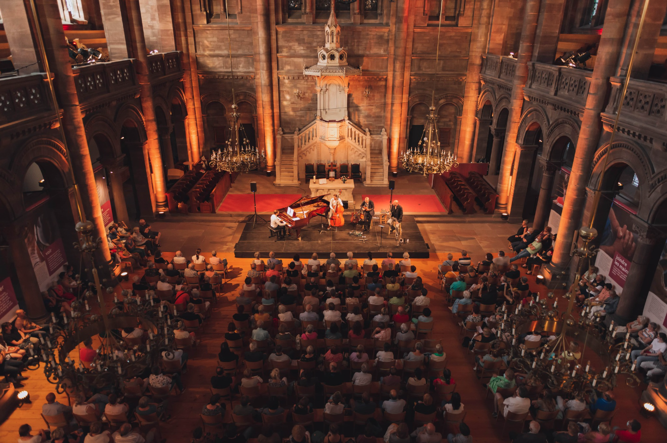 Vue d'en haut de la salle de l'Eglise du temple Neuf à Strasbourg. Des musiciens sont éclairés devant une salle pleine de personnes, assises.