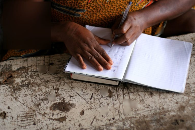 Une femme noire prend des notes, on ne voit que ses mains et son cahier