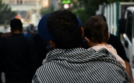 Un homme de dos avec un foulard porte son enfant dans les bras
