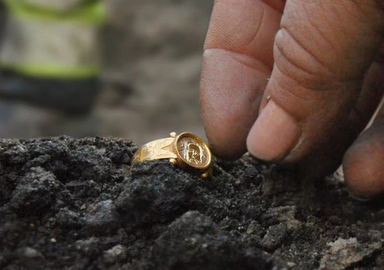 Des doigts sortent une bague en or de la terre