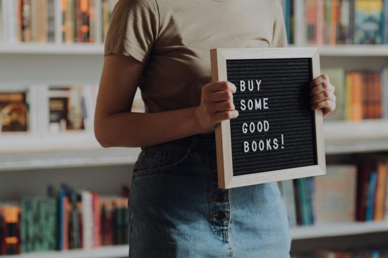 Une femme tient une pancarte dans une libraire avec l'inscription "Achetez de bons livres!" en anglais