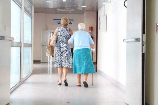 Deux personnes de dos marchent dans un couloir d'hôpital, l'une d'elle se déplace avec une canne et