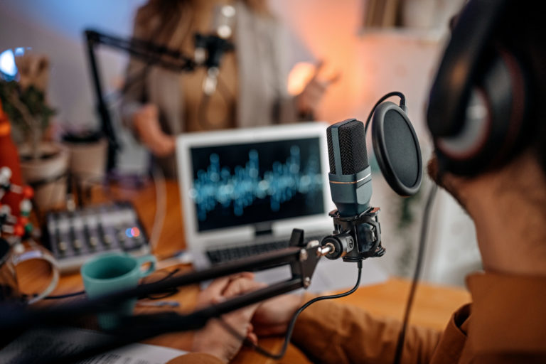 Une personne de dos parle dans un micro dans un studio sous la forme d'un podcast ou sous format radio