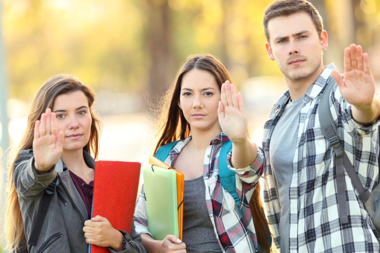 Trois personnes avec la main en avant pour dire stop. Elles portent des sacs à dos et des classeurs.