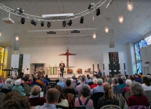 Le directeur de Wycliffe Suisse, Peter Wilburg, s'adresse à un auditoire dans une salle comble. Il est sur une estrade et parle dans un micro.
