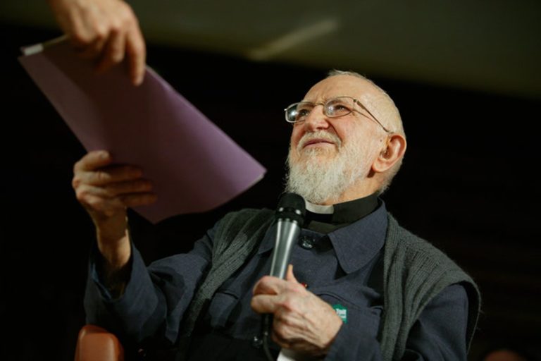 L'abbé Pierre avec un micro dans une main et un dossier violet dans l'autre