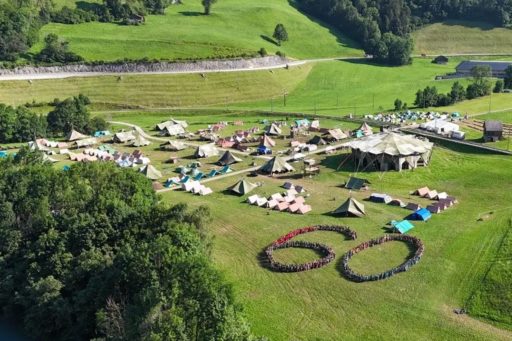 Vue aérienne du camp scout de la Brigade romande des Flambeaux de l'Evangile avec des tentes et des personnes regroupées qui forment le chiffre 60, pour les 60 ans de la brigade
