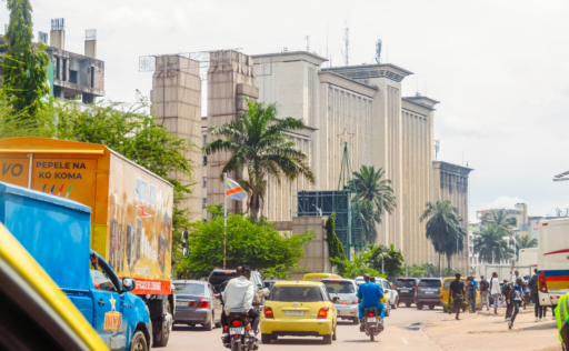 Une large avenue dans la ville de Kinshasa. Il y a peu de trafic et il fait très clair.