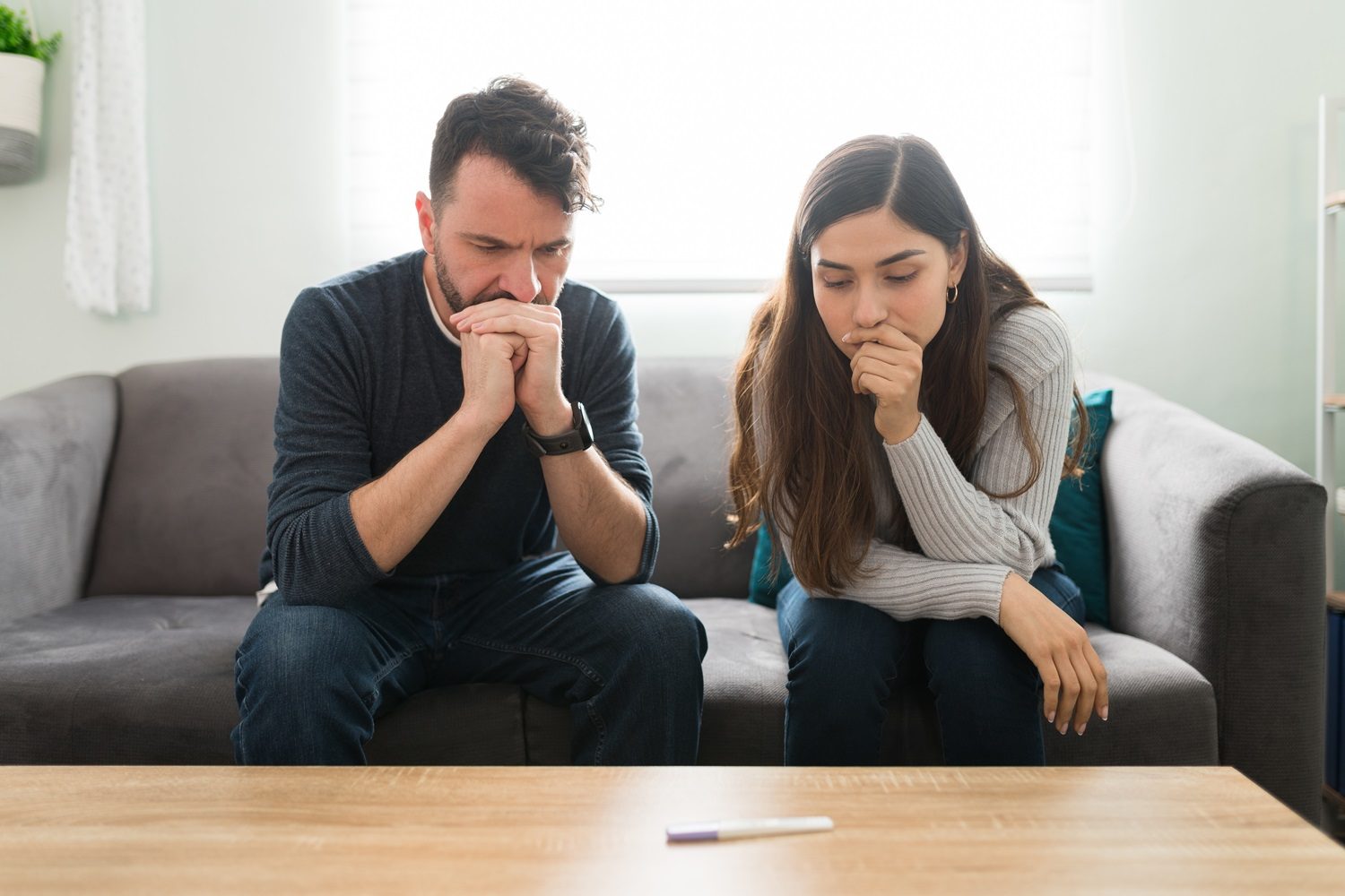 Un couple anxieux assis dans le canapé regarde un test de grossesse posé sur la table