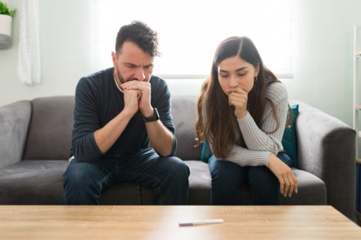 Un couple anxieux assis dans le canapé regarde un test de grossesse posé sur la table