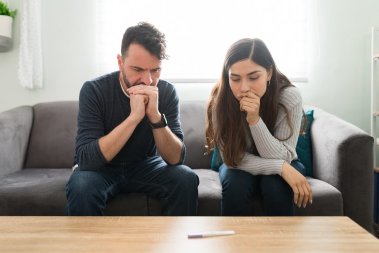 Un couple anxieux assis dans le canapé regarde un test de grossesse posé sur la table
