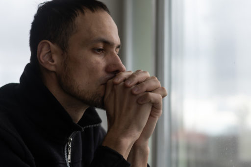 Un homme a ls mains jointes devant son visage, comme s'il priait. Mais il a les yeux ouverts et semble surtout réfléchir.