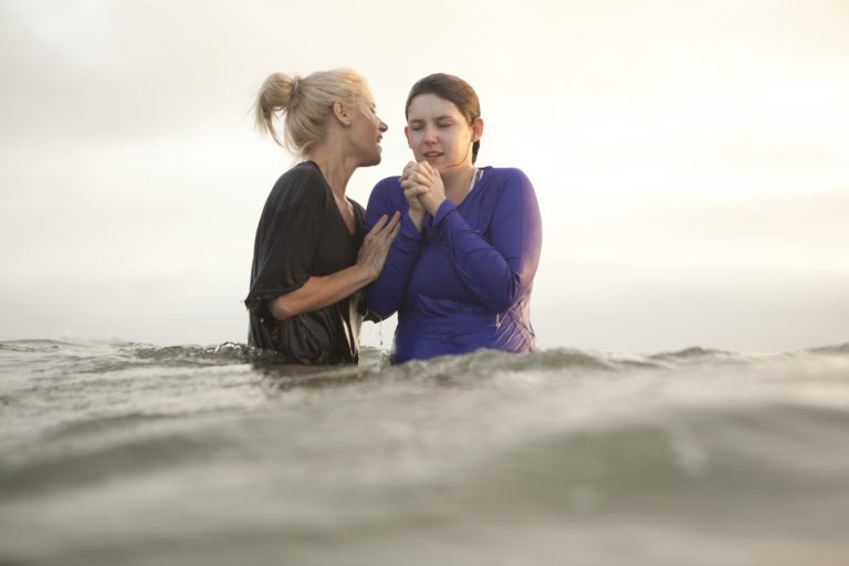 Une femme baptise une jeune fille dans l'eau, en extérieur