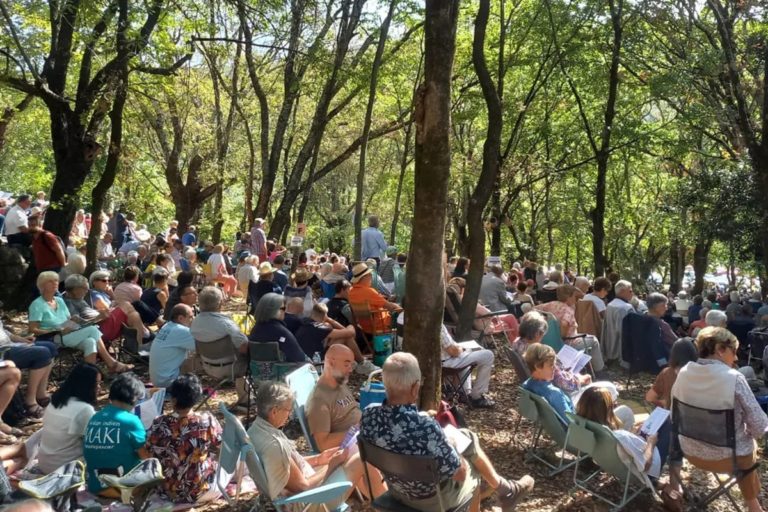 Des personnes assises sous l'ombre des arbres assistent à l'Assemblée du Désert,