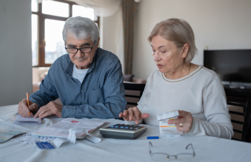 Un couple âgé calcule son budget. L'homme et la femme sont assis à table, avec une calculette et plusieurs documents.