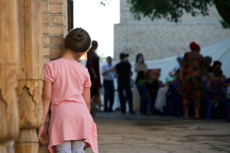Une jeune fille, cachée derrière un bâtiment observe au loin un groupe d'adultes