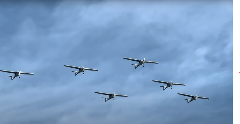 Six avions électriques volent en formation. Le ciel est nuageux.