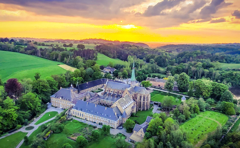 Vue aérienne de l'abbaye du Val-Dieu au crépuscule. Elle comporte une église, une basilique et d'autres bâtiments.