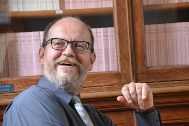 Didier Halter souriant avec une bibliothèque remplie de livres en arrière plan