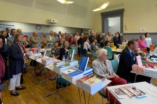 Des auteurs et autrices assis derrière des tables où sont exposés leurs livres