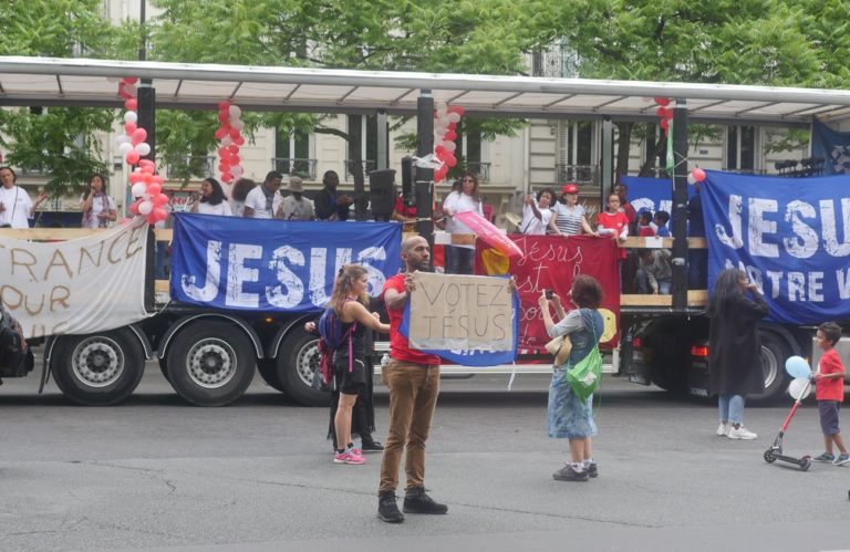 Un camion avec des banderoles Jésus et un homme devant tient une pancarte "Votez Jésus"
