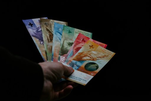 Une main tend des billets suisses de différentes couleurs