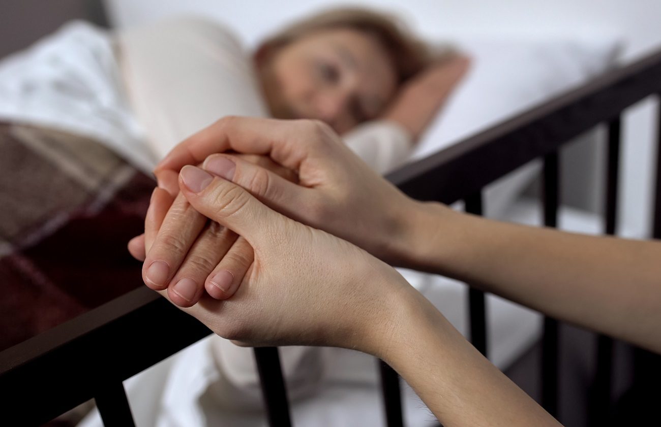 Une femme allongée sur un lit, des mains lui caressent sa main