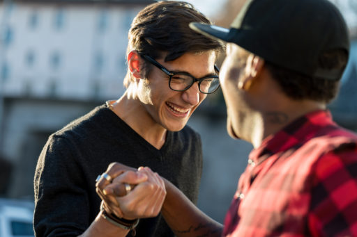 Deux jeunes hommes se serrent la main en signe d'amitié, en extérieur. Ils rient.