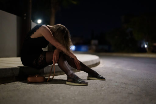 Une prostituée est assise sur un trottoir, la tête baissée sur ses bras. Il fait nuit et elle a l'air malheureux ou ivre.