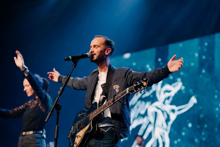 Thomas Pouzin, guitariste de Glorious, se tient sur scène les bras étendus et yeux fermés, en adoration.