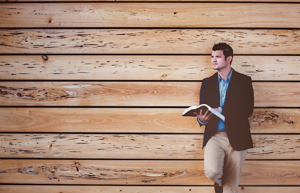 Un homme debout, adossé à des planches en bois, tient dans sa main une Bible et a le regard fixé vers l'horizon