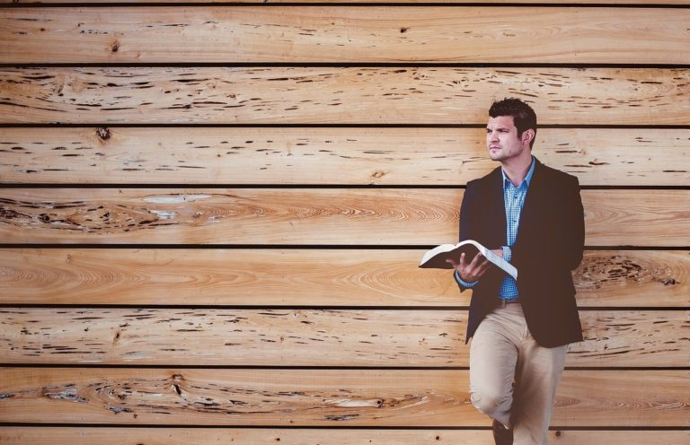 Un homme debout, adossé à des planches en bois, tient dans sa main une Bible et a le regard fixé vers l'horizon