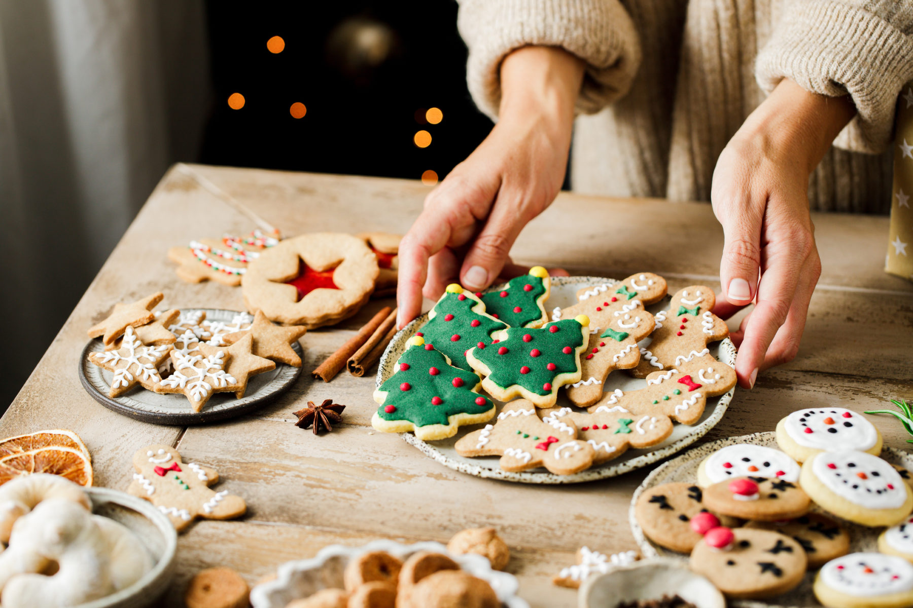 Une femme pose une assiette de biscuits de Noêl sur une table, à côté d'autres pâtisseries.