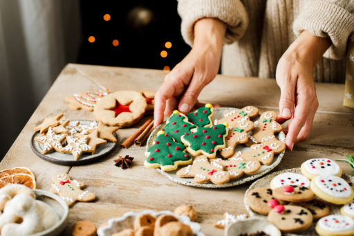 Une femme pose une assiette de biscuits de Noêl sur une table, à côté d'autres pâtisseries.